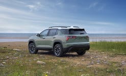 A green SUV parked on a rocky coastline with a clear blue sky and ocean in the background.