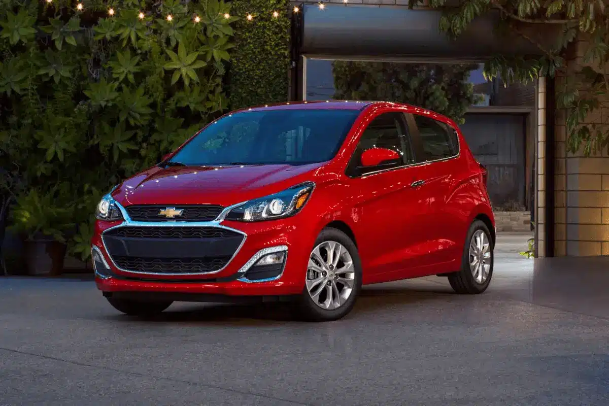 Red car parked in a cozy courtyard with string lights, surrounded by lush greenery and a stylish patio.