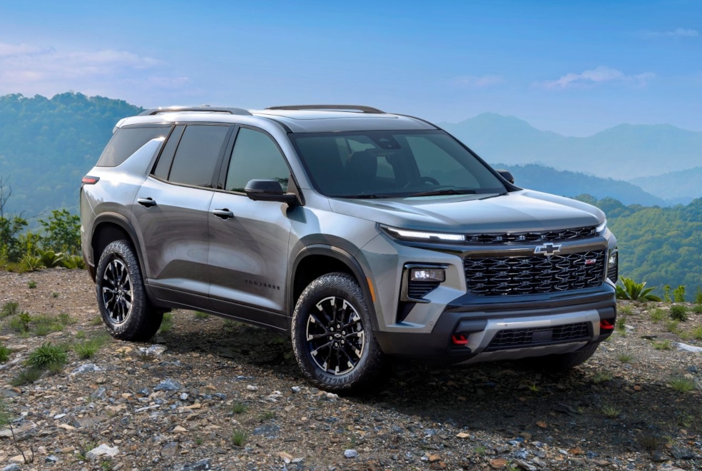 Silver SUV on a rocky terrain with lush green hills and a clear blue sky in the background.