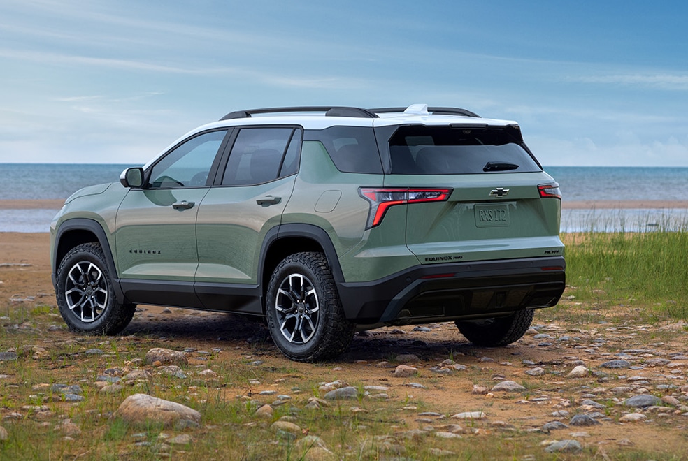 Green SUV parked on a rocky beach with grass and ocean in the background, showcasing its design.