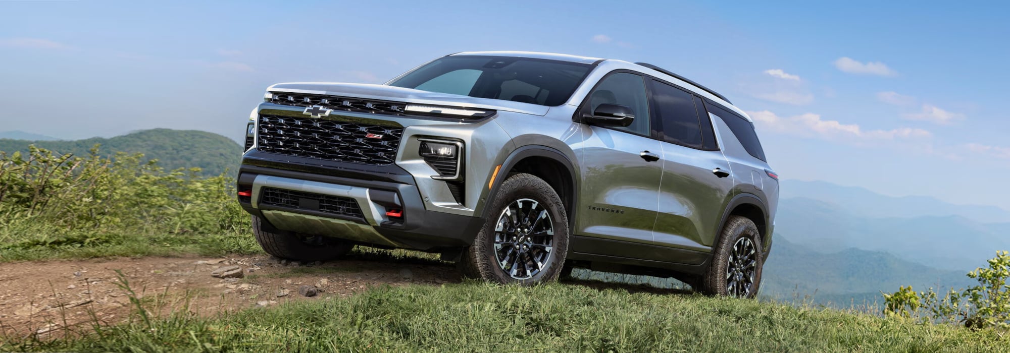 Silver SUV parked on a grassy hill with a mountainous backdrop under a clear sky.