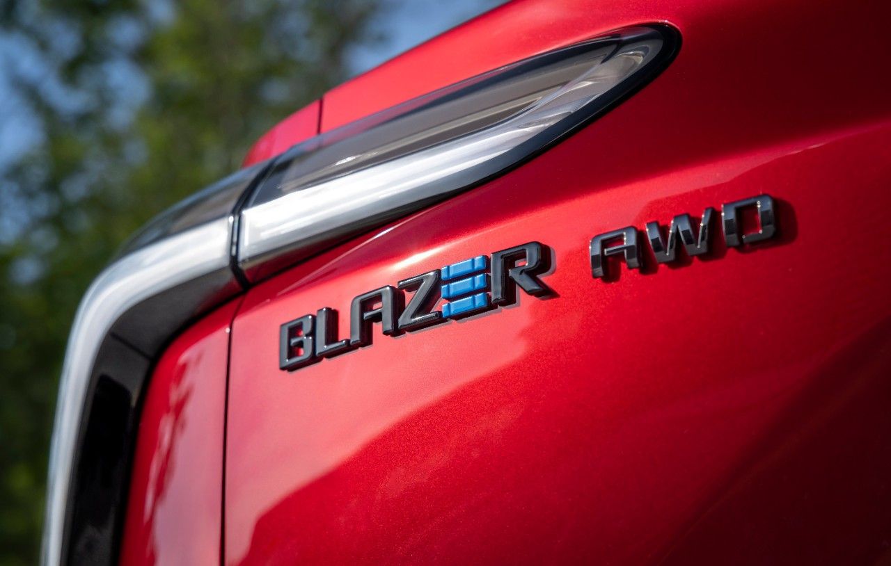 Close-up of a red Chevrolet Blazer AWD badge and taillight detail against a blurred green background.