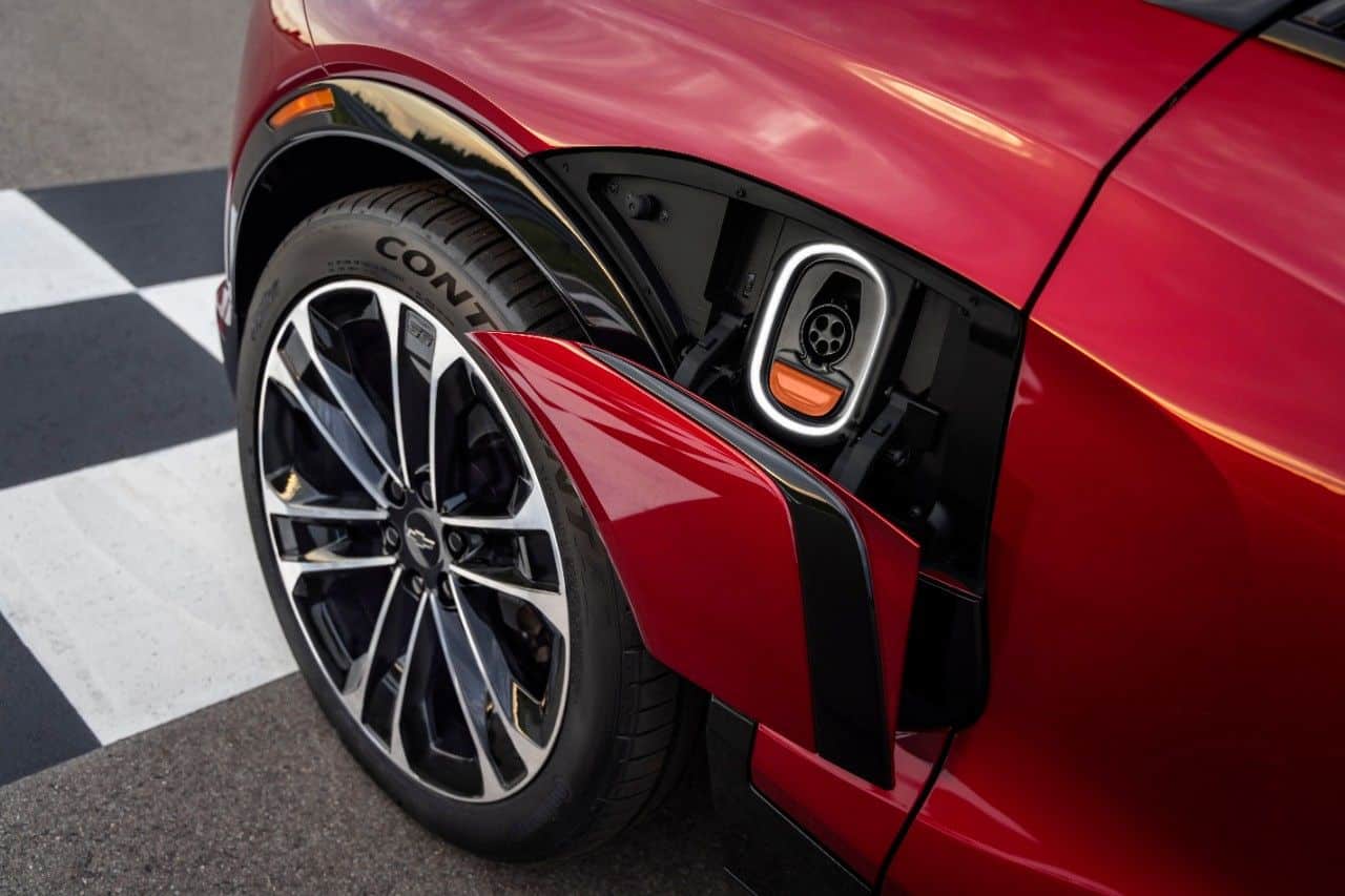 Red electric vehicle with an open charging port, showcasing the wheel and part of a charging station.