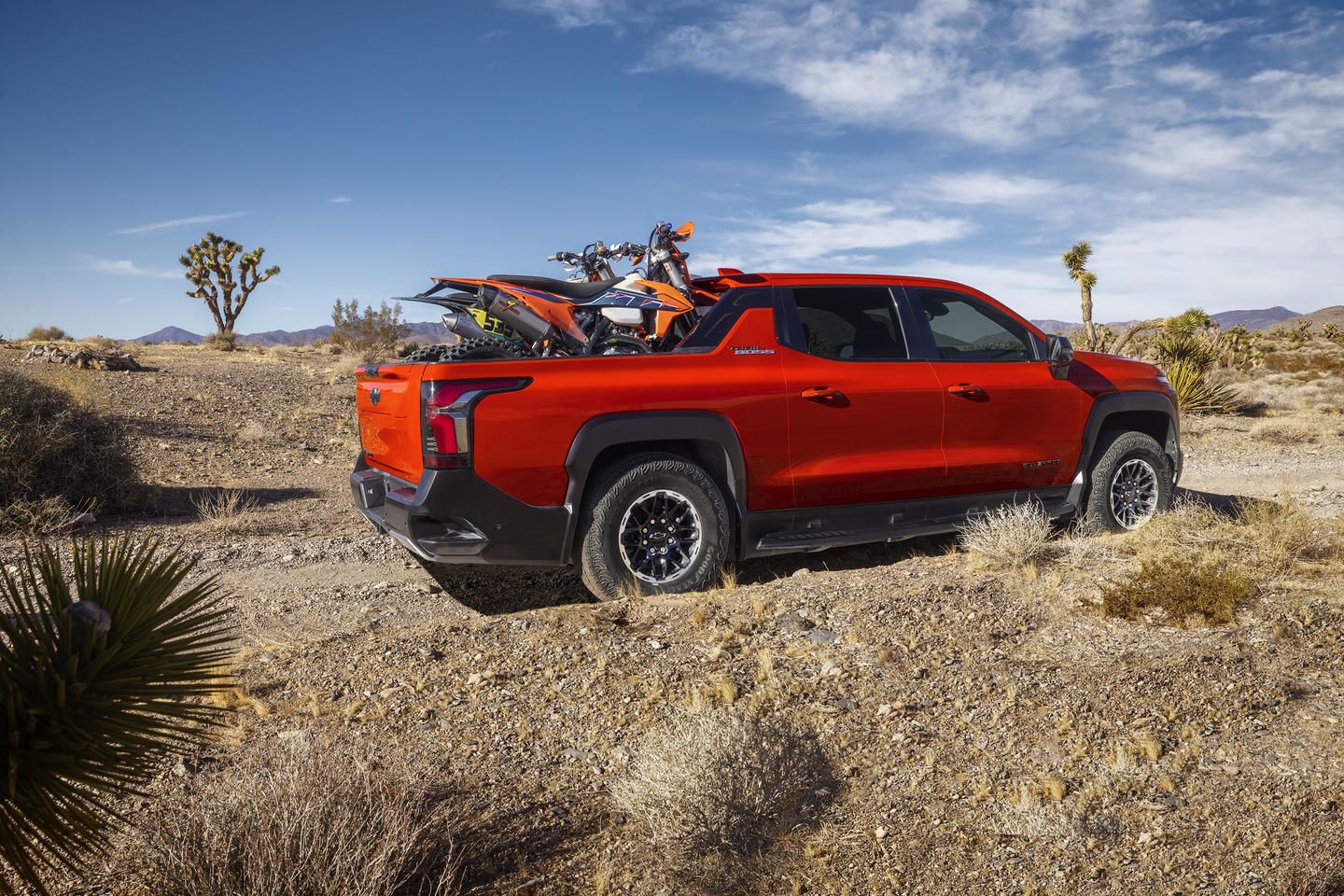 Red truck with a motorcycle in the bed parked in a desert landscape with blue sky.