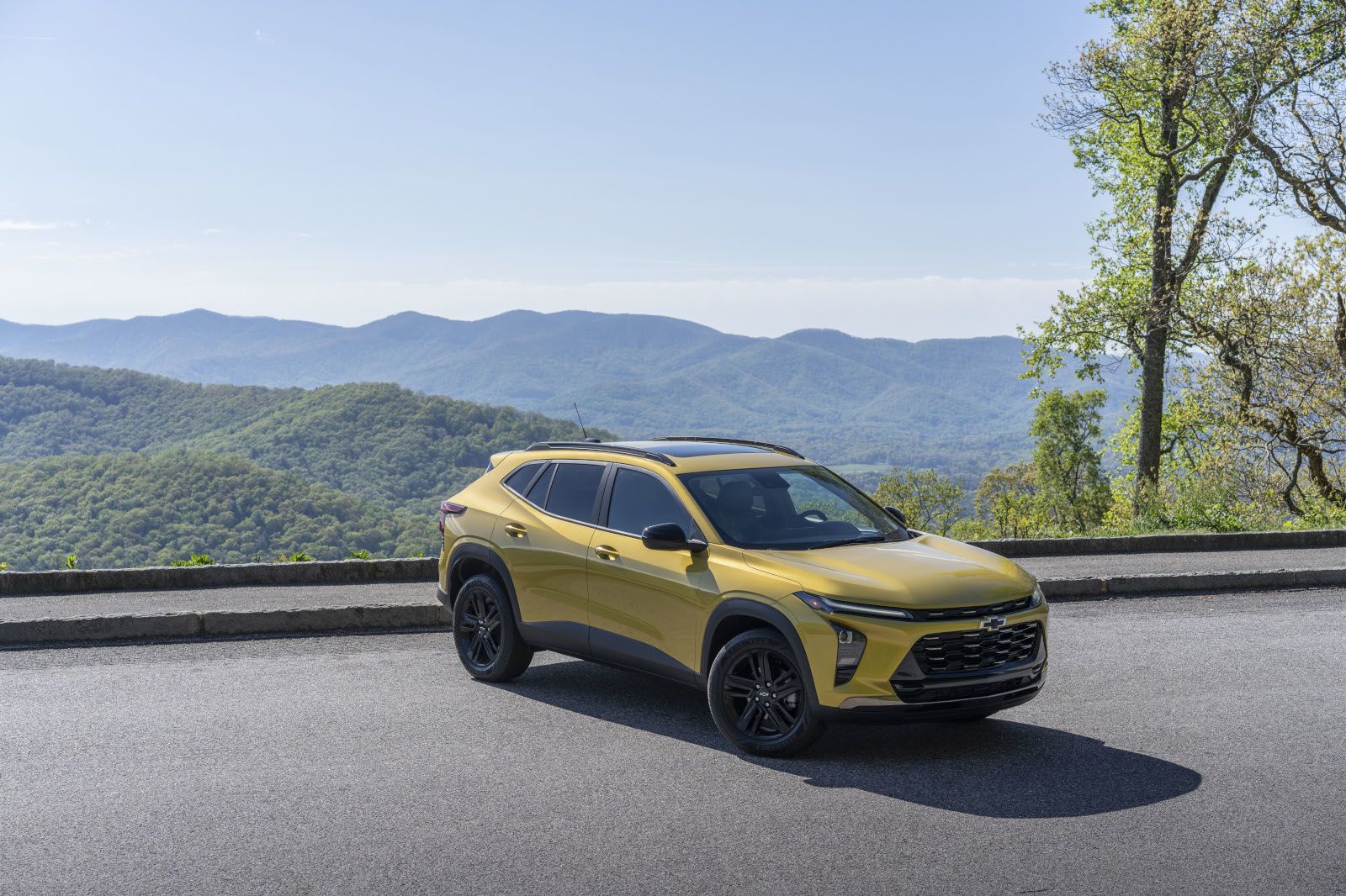 Yellow SUV parked on a scenic mountain road with lush green hills in the background.