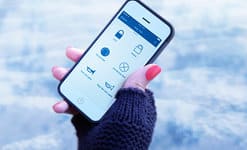 A hand with red nails holds a smartphone displaying a security app interface with icons against a snowy background.