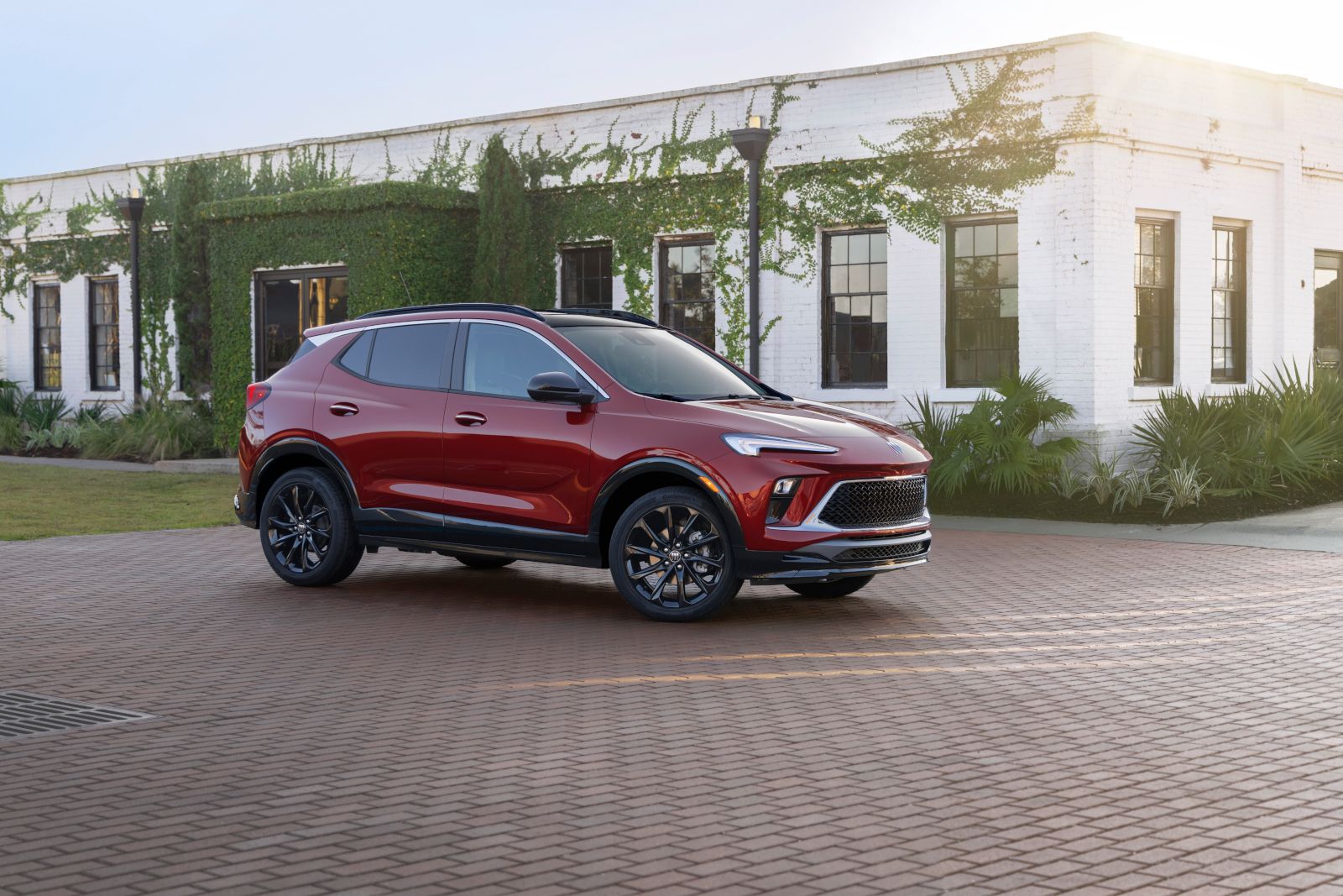 Red SUV parked on brick driveway, with greenery-covered white building in background.