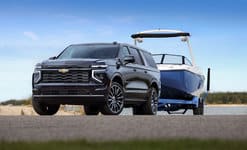 SUV towing a blue boat on a road with clear skies in the background.