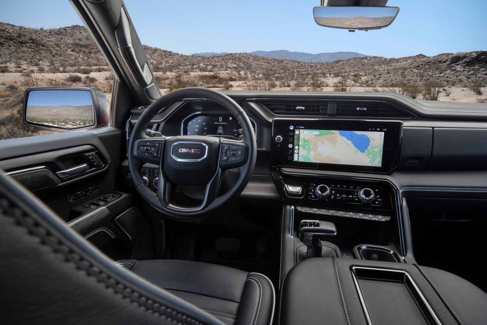 Interior view of a GMC vehicle with a steering wheel and a central touchscreen displaying a map, set against a desert backdrop.