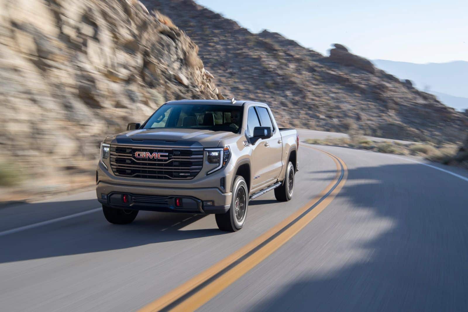 GMC pickup truck driving on a winding road near rocky terrain.