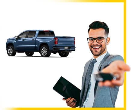 Man in suit holding car keys with a parked blue pickup truck in the background, suggesting auto sales.