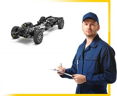 Mechanic in blue uniform with clipboard stands beside a car chassis model, suggesting vehicle inspection.