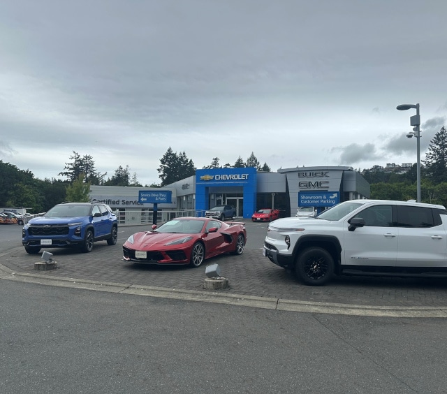Cars displayed outside a Chevrolet Buick GMC dealership, including a blue SUV, red sports car, and white pickup.
