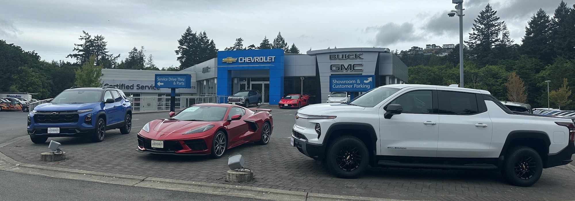 Cars displayed outside a Chevrolet Buick GMC dealership, including a blue SUV, red sports car, and white pickup.